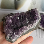 Amethyst crystal cluster held in a hand with a blurred background