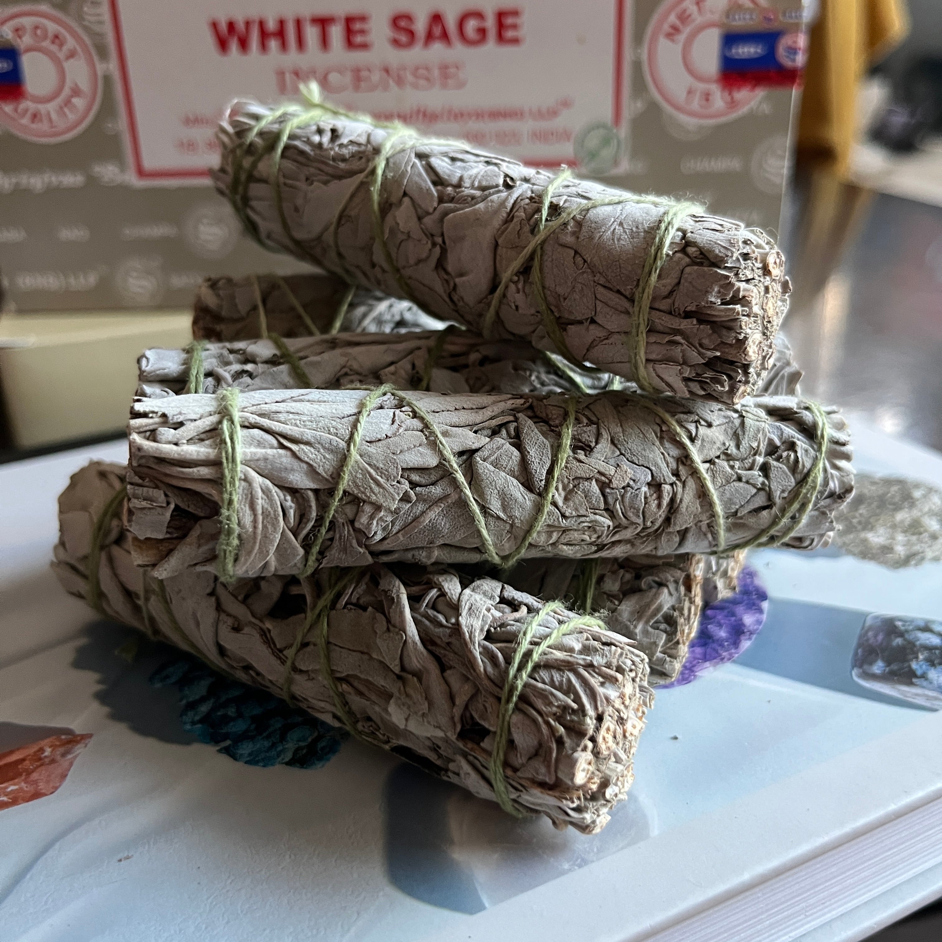 Stack of white sage smudge sticks on a white surface with a box in the background.