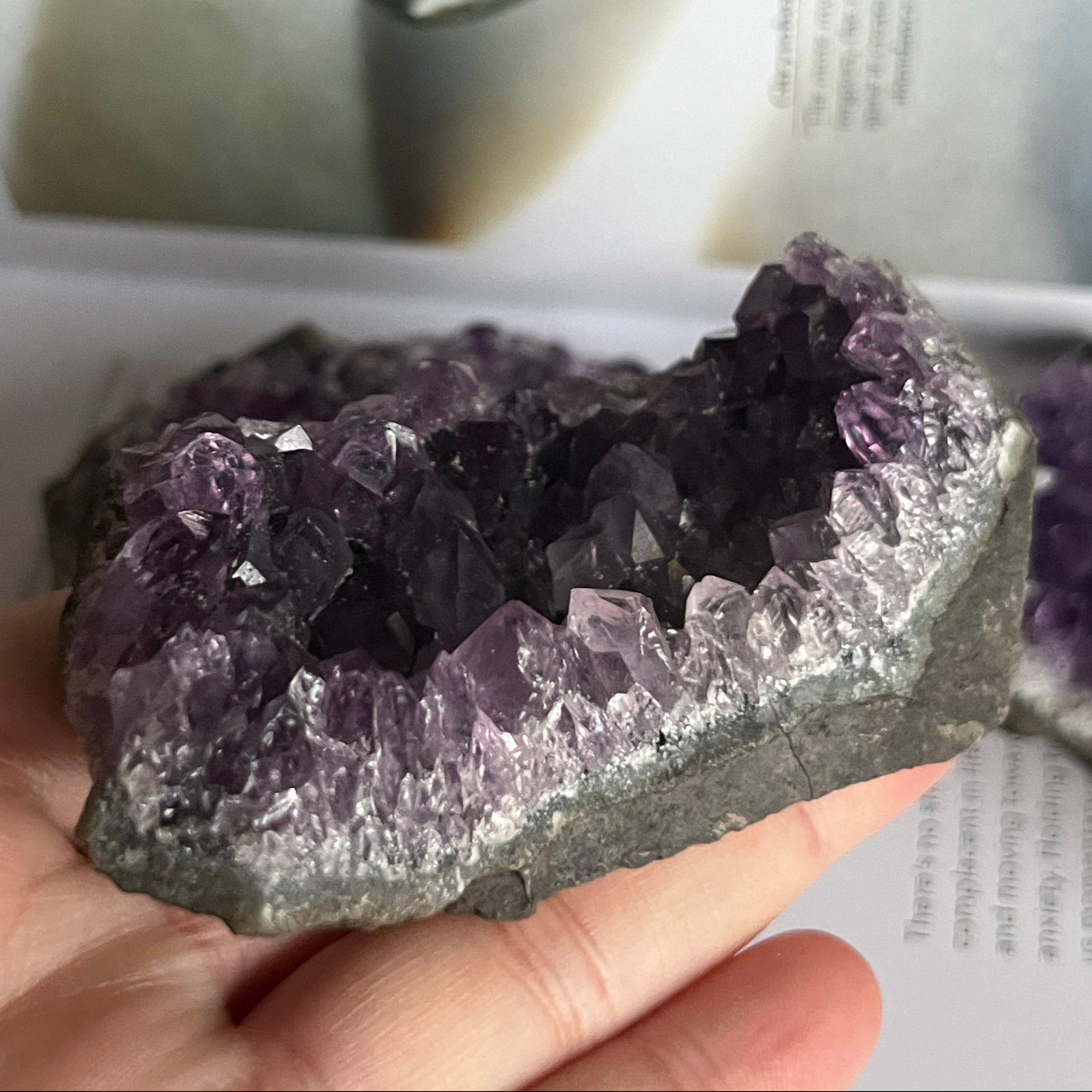 Amethyst crystal cluster held in a hand with a blurred background