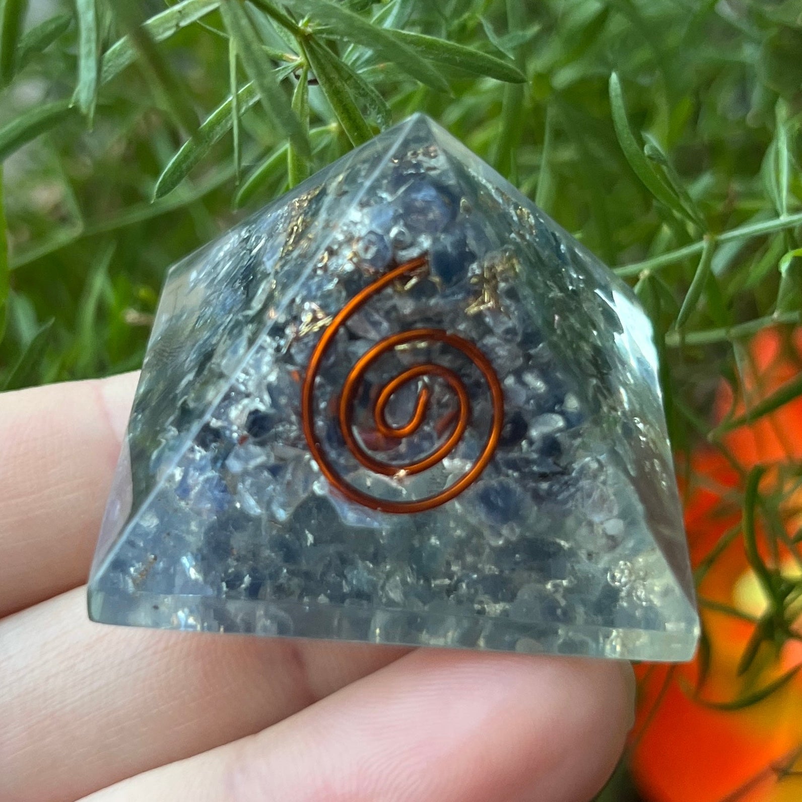 sapphire orgone pyramid with a copper spiral design held by a hand against a natural background