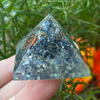 sapphire orgone pyramid with a copper spiral design held by a hand against a natural background