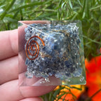 sapphire orgone pyramid with a copper spiral design held by a hand against a natural background