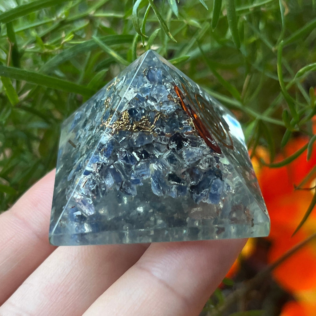 sapphire orgone pyramid with a copper spiral design held by a hand against a natural background