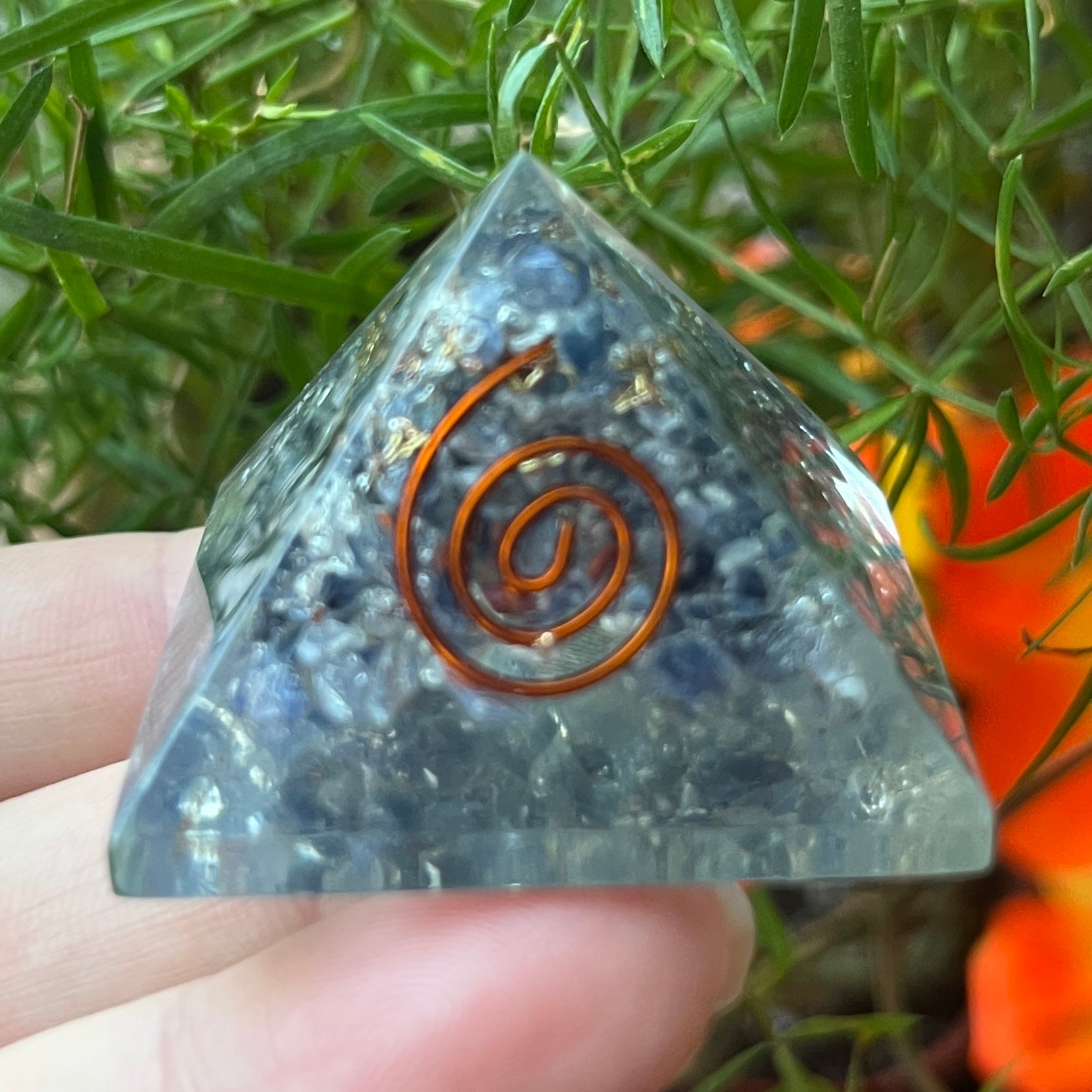 sapphire orgone pyramid with a copper spiral design held by a hand against a natural background