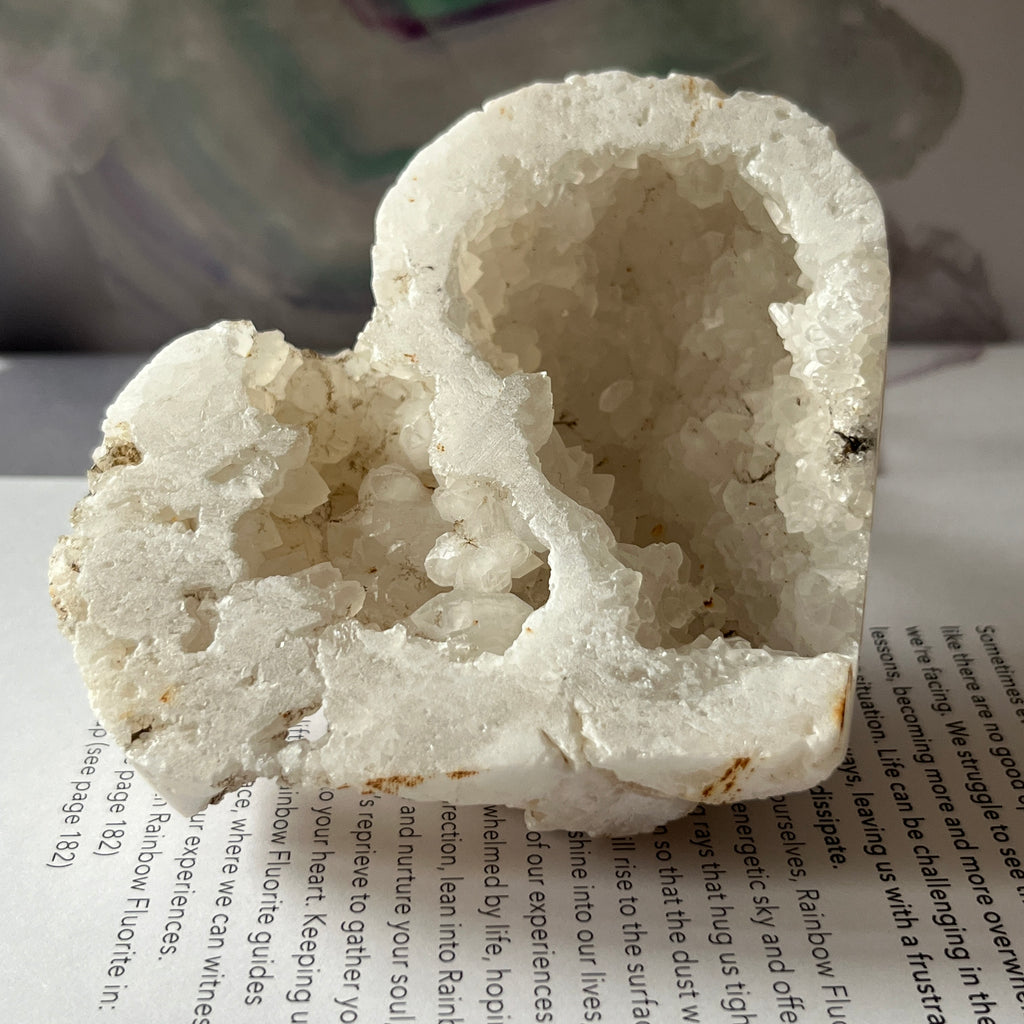 Heart-shaped white crystal geode held by a hand on an open book