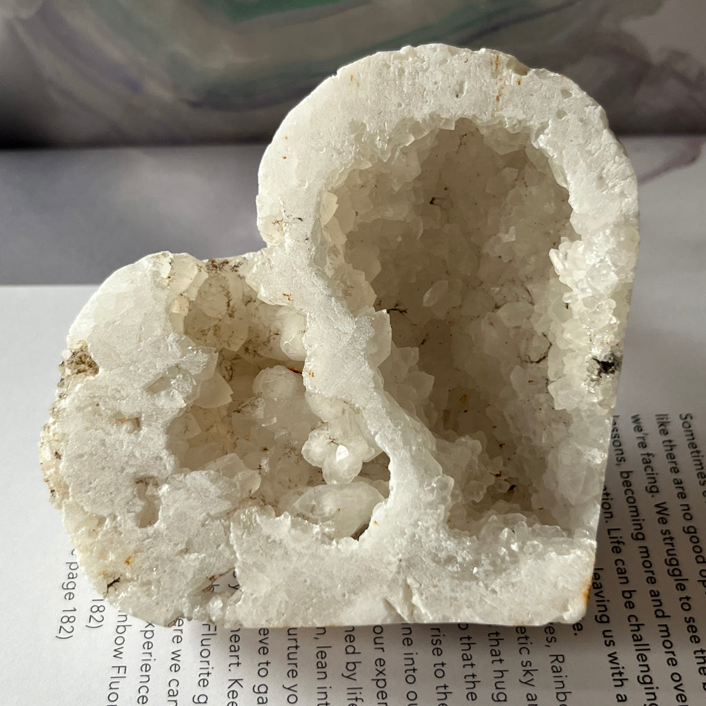 Heart-shaped white crystal geode held by a hand on an open book