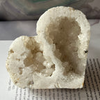 Heart-shaped white crystal geode held by a hand on an open book
