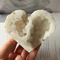 Heart-shaped white crystal geode held by a hand on an open book