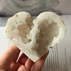 Heart-shaped white crystal geode held by a hand on an open book