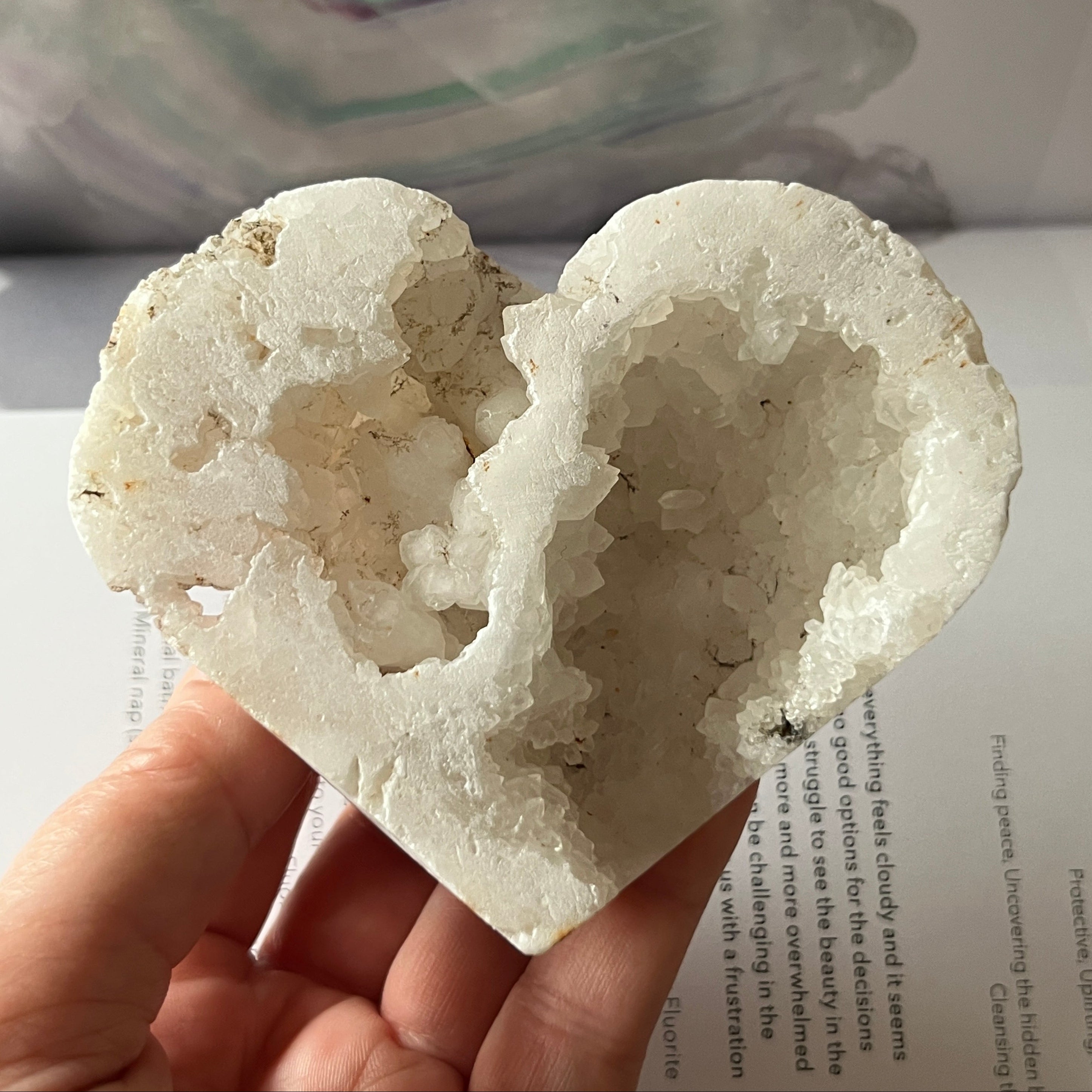 Heart-shaped white crystal geode held by a hand on an open book