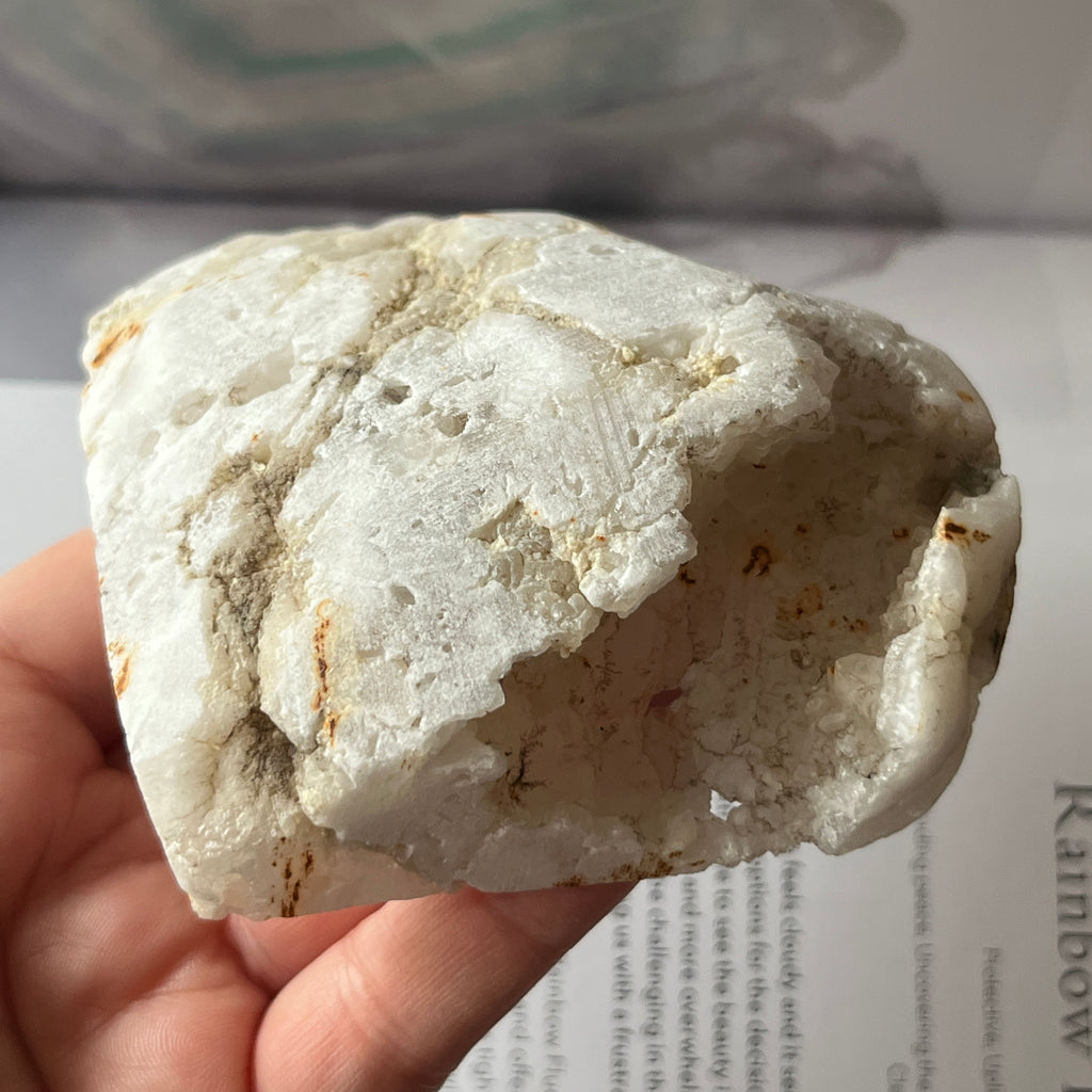 Heart-shaped white crystal geode held by a hand on an open book
