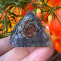 sapphire orgone pyramid with a copper spiral design held by a hand against a natural background