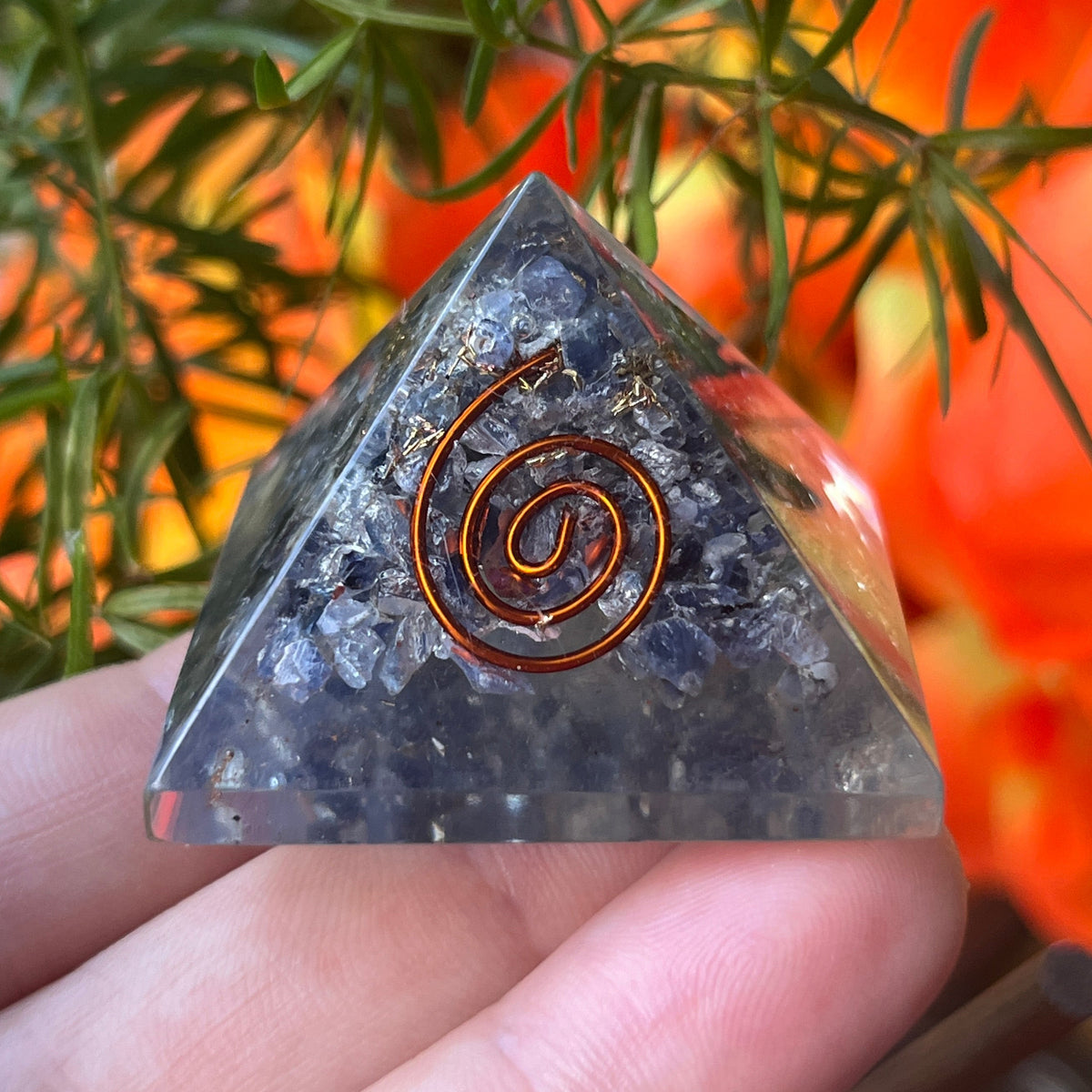sapphire orgone pyramid with a copper spiral design held by a hand against a natural background