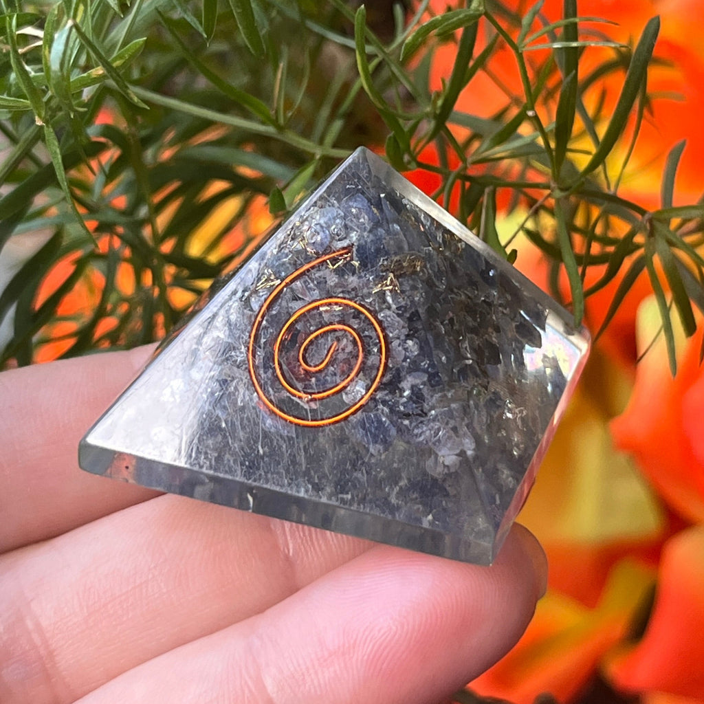 sapphire orgone pyramid with a copper spiral design held by a hand against a natural background