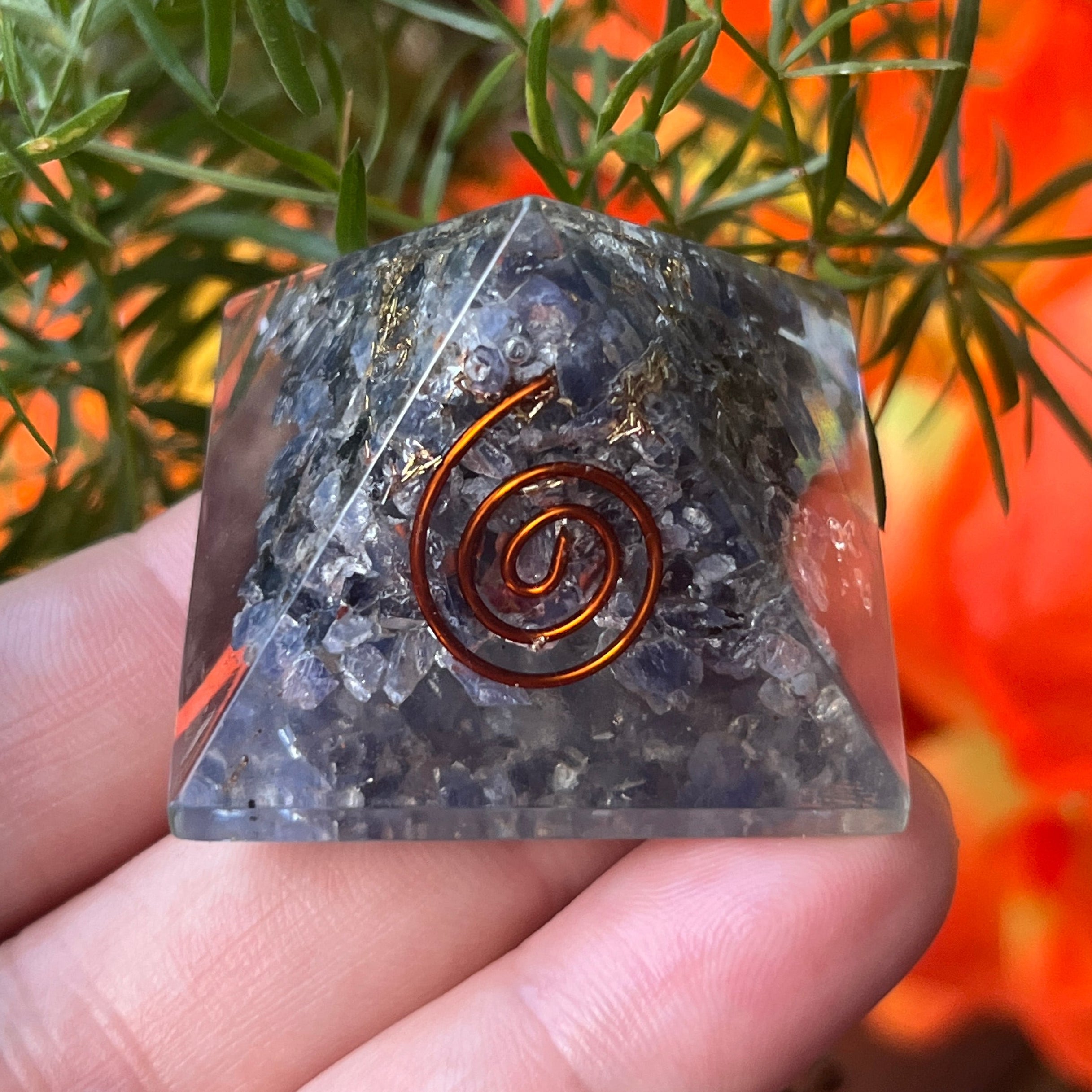 sapphire orgone pyramid with a copper spiral design held by a hand against a natural background